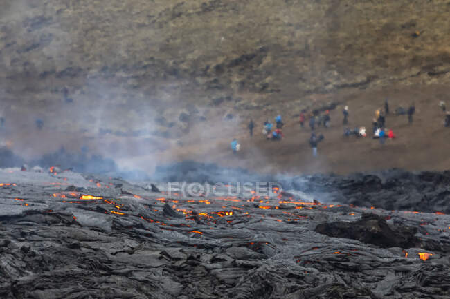 Magma close-up faíscas para fora do buraco do vulcão na Islândia, enquanto você vê as pessoas olhando para os rios de lava — Fotografia de Stock