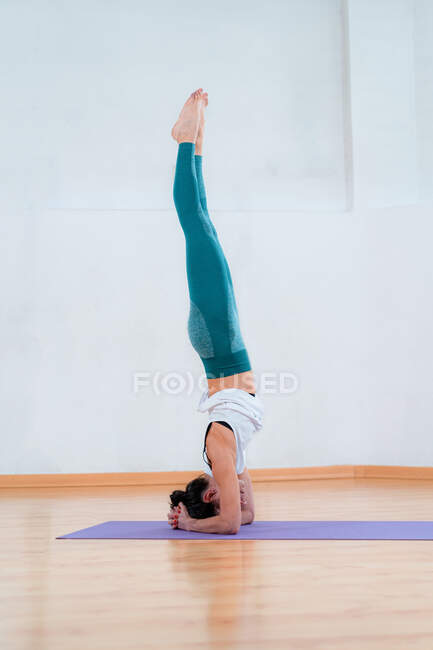 Seitenansicht einer anonymen flexiblen Frau in Sportbekleidung, die mit erhobenen Beinen auf dem Kopf steht, während sie im Haus Yoga praktiziert — Stockfoto