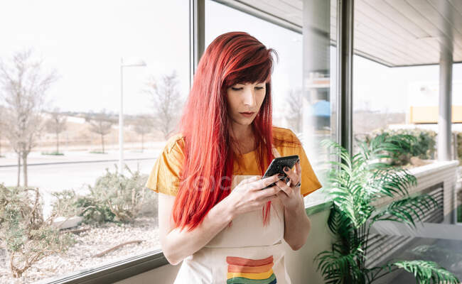 Jeune femme homosexuelle avec des cheveux teints dans le tablier de messagerie texte sur téléphone portable dans la maison légère — Photo de stock