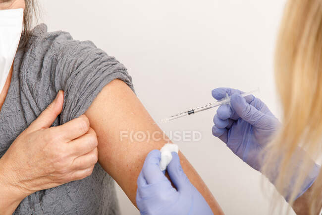 Crop female medical specialist in protective uniform and latex gloves vaccinating senior female patient in clinic during coronavirus outbreak — Stock Photo