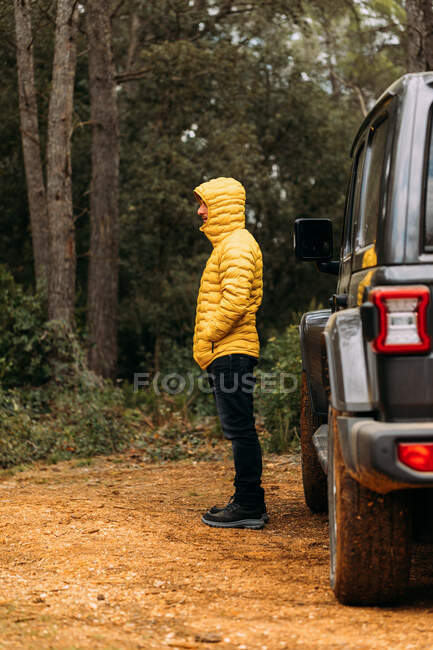 Vue latérale de l'aventurier à côté de sa voiture hors route regardant la route dans la montagne — Photo de stock
