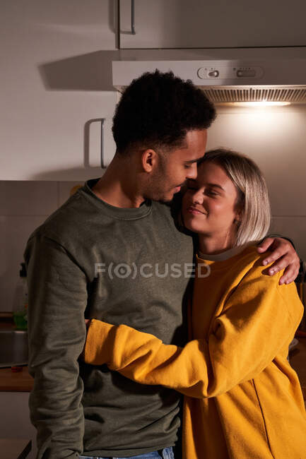 Gentile coppia multietnica che abbraccia in cucina accogliente e godersi la serata a casa insieme — Foto stock
