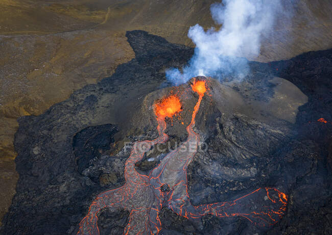 Desde arriba el magma sale del agujero del volcán y corre como ríos de lava sobre el suelo en Islandia - foto de stock