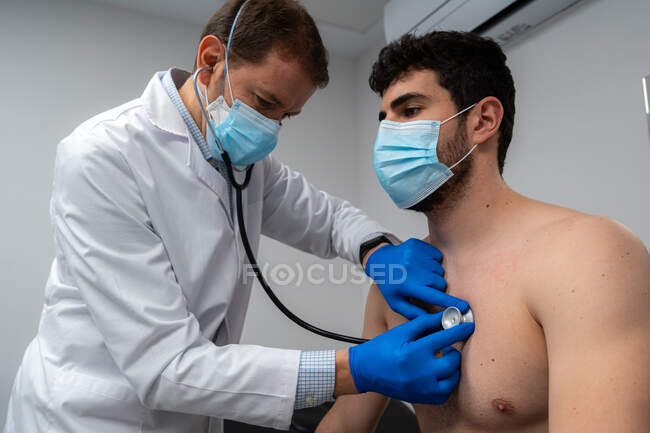 Низький кут пацієнта в масці з використанням фонендоскопа при вивченні легенів пацієнта в масці в лікарні — стокове фото