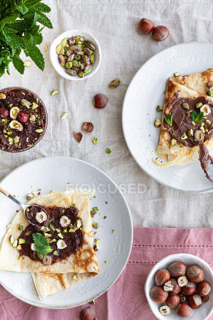 Vista dall'alto di deliziose crepes guarnite con cioccolato e noci servite sul piatto a colazione — Foto stock