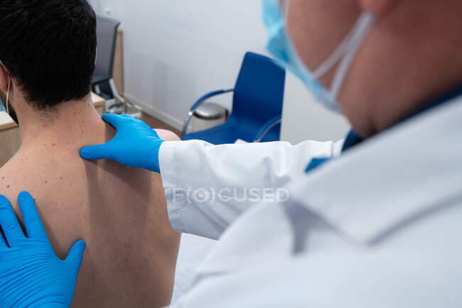 Cropped irreconhecível profissional quiroprático masculino examinando costas do paciente em máscara durante a consulta no hospital — Fotografia de Stock
