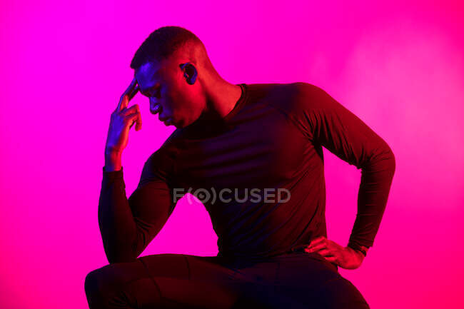 Уверенный молодой черный человек в темном спортивном наряде, держащий лицо  на неоновом розовом фоне в темной студии — красивый, Пондер - Stock Photo |  #466828922