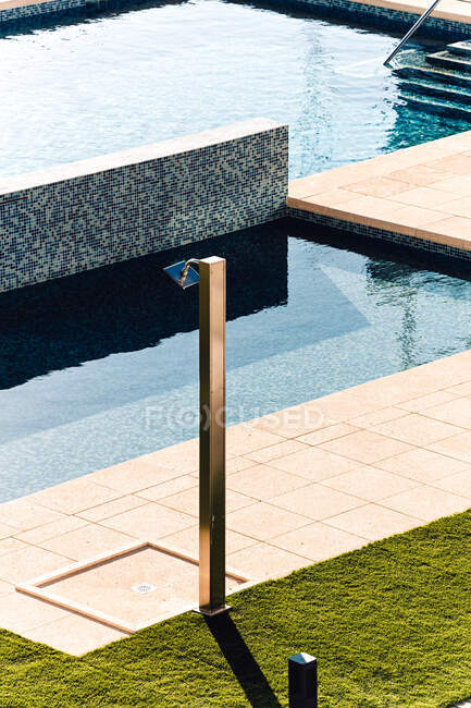 Chuveiro ao ar livre entre gramado e piscina com escadas contra cerca na cidade no dia ensolarado — Fotografia de Stock