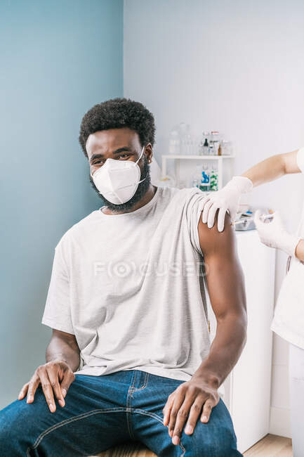 Cropped unrecognizable female medical specialist in protective uniform, latex gloves and face mask vaccinating African American man patient in clinic during coronavirus outbreak — Stock Photo