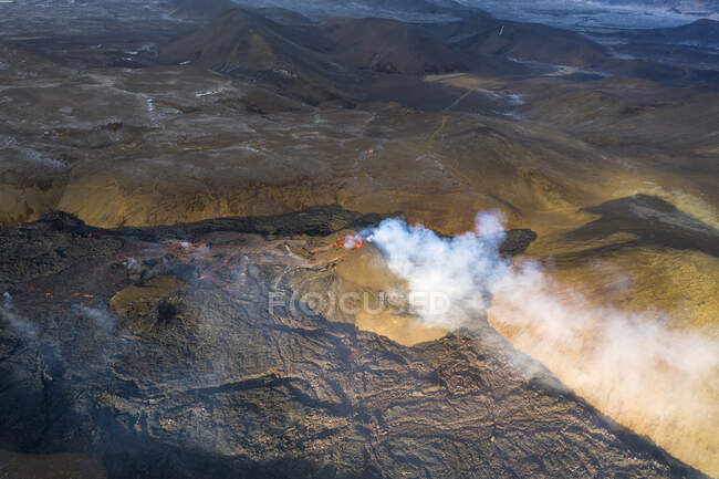 З верхніх колон диму й магми вилітають з вулканічної ями й біжать, немов річки лави над землею в Ісландії. — стокове фото
