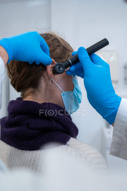 Otorinolaringoiatra maschio in maschera e guanti che controlla le orecchie del paziente con otoscopio durante l'appuntamento in ospedale — Foto stock