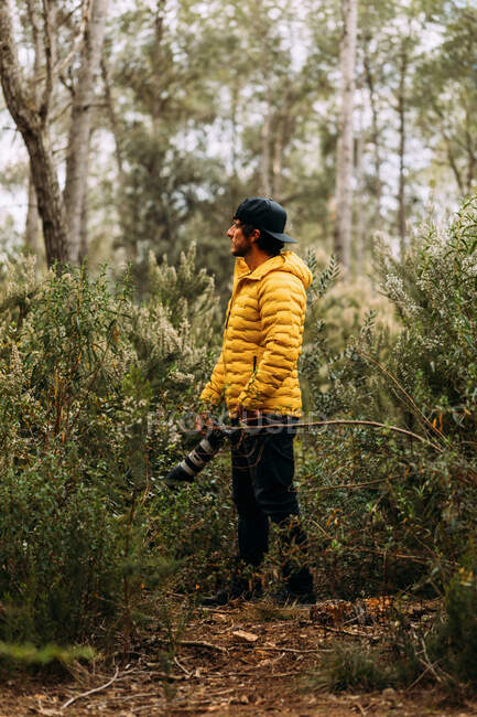 Vista laterale di un fotografo in berretto e giacca gialla in montagna guardando altrove — Foto stock