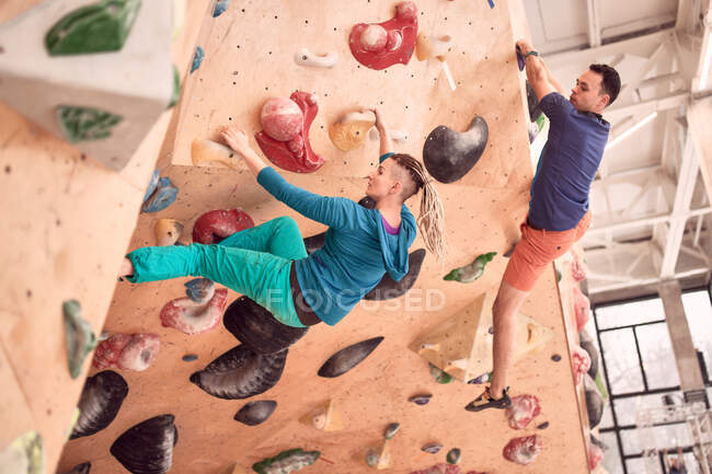 Side view of strong male and female climbers climbing artificial wall in bouldering club — Stock Photo