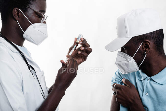 Ethnische Ärztin füllt Spritze aus Flasche mit Impfstoff zur Impfung eines afroamerikanischen Patienten in einer Klinik während des Coronavirus-Ausbruchs — Stockfoto