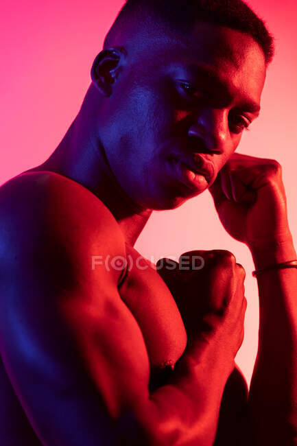 Confiante jovem atlético preto cara com torso nu olhando para a câmera com as mãos apertadas em punhos em estúdio no neon rosa fundo — Fotografia de Stock