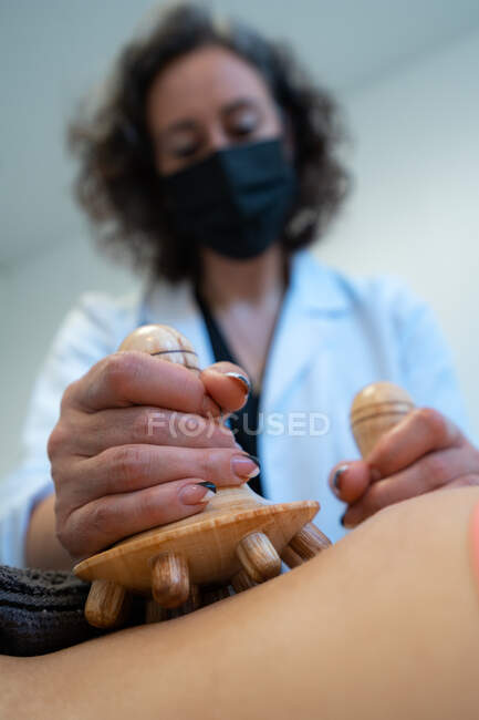Обрезанный анонимный массажист с помощью деревянного инструмента и массирующего живота женщины во время ухода за телом в клинике — стоковое фото