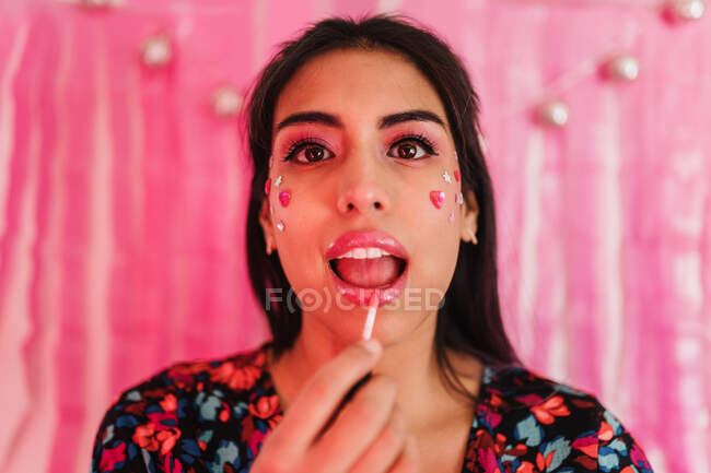 Portrait of a brunette woman with makeup and painting her lips with a pink background — Stock Photo