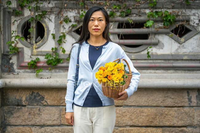 Das Mädchenporträt der schönen Asiatin, während sie einen Weidenkorb mit gelben Blumen trägt. — Stockfoto