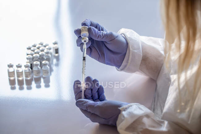 Неузнаваемый медик в защитной маске и латексных перчатках с флаконом коронавирусной вакцины и шприцем, показываемым на камеру, стоя в больничной палате — стоковое фото