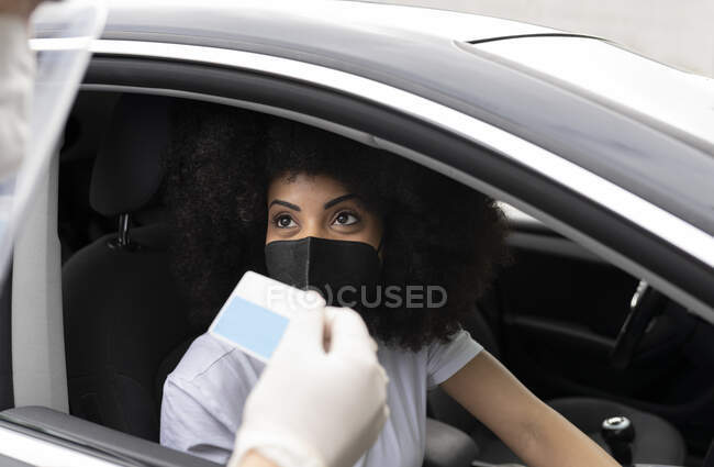 Cropped unrecognizable doctor in protective uniform, latex gloves and face shield checking African American female patient Identification card before vaccine procedure inside the car on a drive through mobile clinic during coronavirus outbreak — Stock Photo