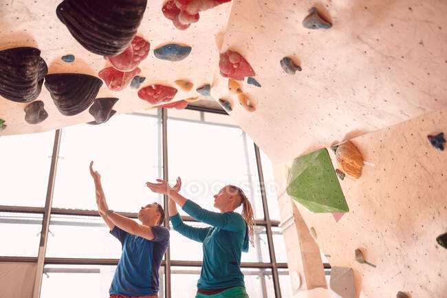 Low angle of male and female climbers practicing in bouldering center near climbing wall — Stock Photo