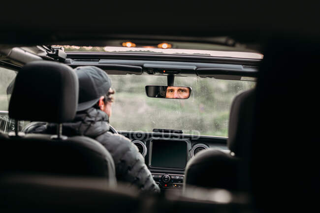 Visão traseira do homem barbudo dirigindo carro e olhando para a câmera através do espelho retrovisor interior — Fotografia de Stock