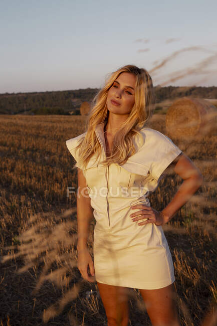 Peaceful female in elegant dress standing on dry field in rural area and looking away — Stock Photo