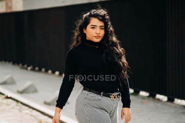 Plus size female wearing trendy cloths standing against black wall in city and looking at camera — Stock Photo