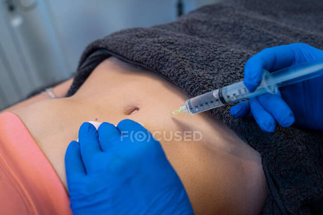 Desde arriba de cultivo anónimo esteticista profesional haciendo inyección para mujer durante el tratamiento de la celulitis en clínica de belleza - foto de stock