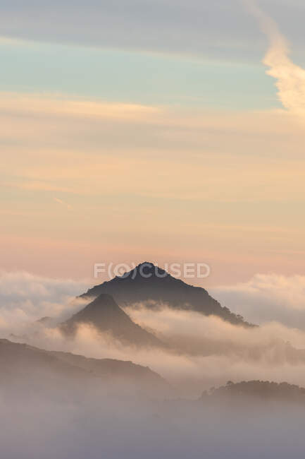 Impresionante paisaje de picos montañosos cubiertos de nubes bajo el colorido cielo del atardecer en el Parque Nacional Sierra de Guadarrama - foto de stock