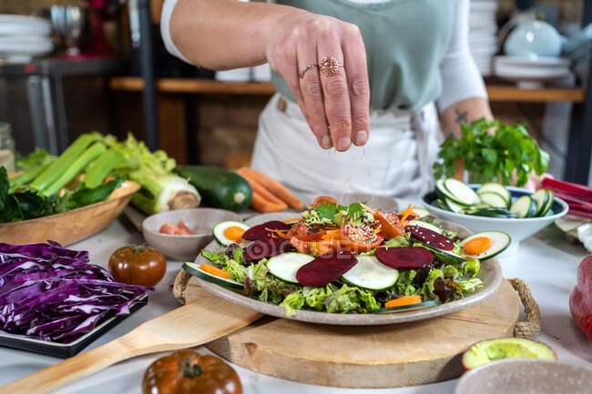Coltiva anonima femmina preparando deliziosa insalata di verdure con semi di sesamo a tavola in cucina di casa — Foto stock