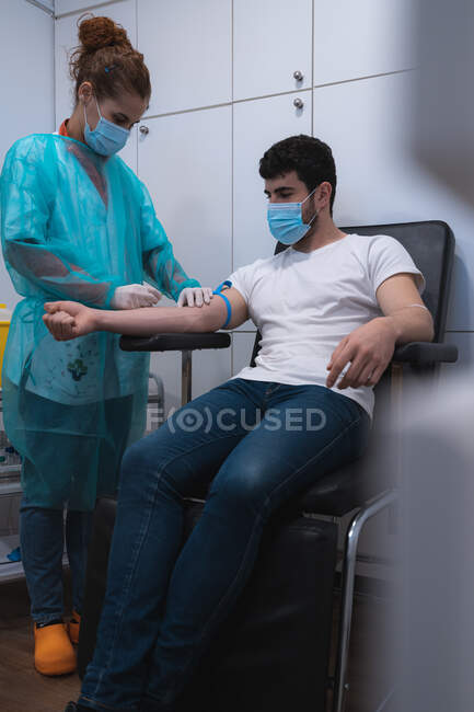 Жіночий лікар у масці, що збирає кров з руки пацієнта, який сидить у медичному кріслі в сучасній клініці — стокове фото