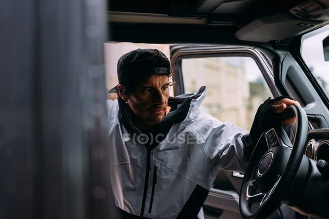 Vista lateral de un hombre con gorra y ropa casual subiendo a un coche - foto de stock