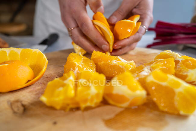 Cortar irreconhecível fêmea descascando laranjas suculentas maduras em tábua de corte de madeira na mesa da cozinha — Fotografia de Stock