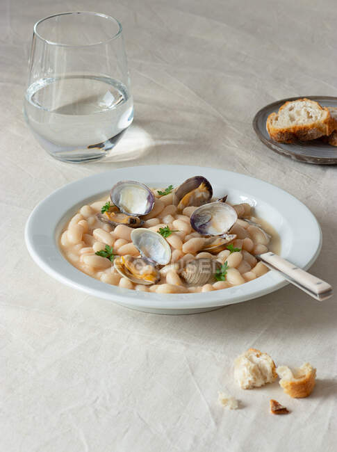 Antipasto tradizionale spagnolo stufato di favette bianche con molluschi in piatto con foglie di prezzemolo fresco sulla tovaglia — Foto stock
