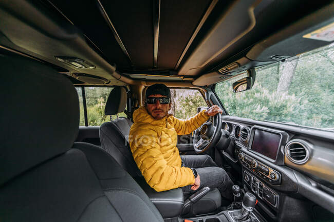 Innenansicht eines Fahrers mit Mütze und Sonnenbrille in einem Geländewagen, der in die Kamera blickt — Stockfoto