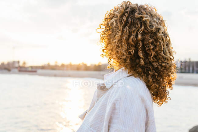 Вид сбоку анонимной этнической женщины с кудрявыми волосами на обочине, восхищающейся живописным закатом летом — стоковое фото