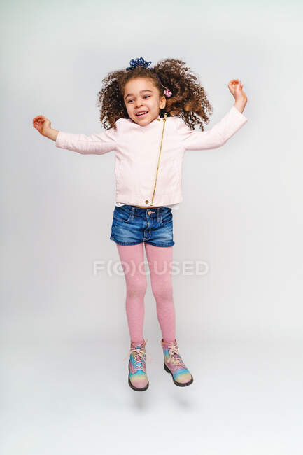 Enfant sympathique avec des cheveux bouclés en short et bottes en denim s'amuser tout en regardant ailleurs — Photo de stock