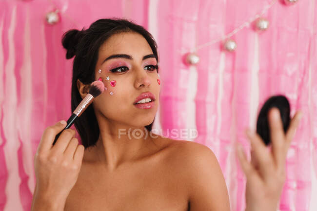 Portrait of a make-up brunette woman putting blush on her face with a pink background — Stock Photo
