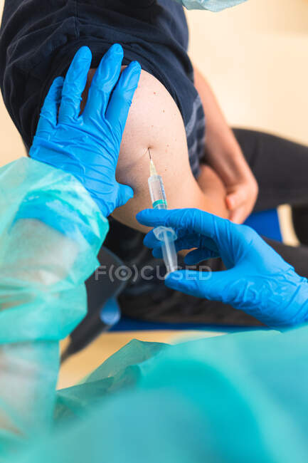 Crop female medical specialist in protective uniform, latex gloves and face mask vaccinating hispanic man patient in clinic during coronavirus outbreak — Stock Photo