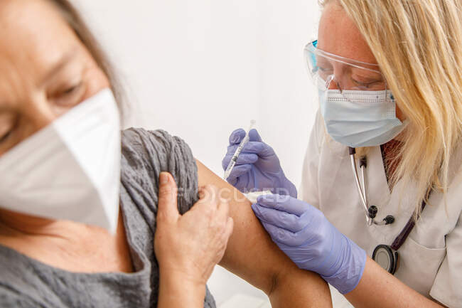 Жіночий медичний фахівець з захисної уніформи та латексних рукавиць вакцинує старших жінок-пацієнтів у клініці під час спалаху коронавірусу. — стокове фото
