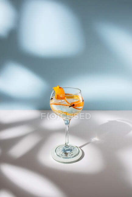 Transparentes Glas Highball-Cocktail mit Zitrusfruchtschale und Nelke gegen Schatten im Sonnenlicht — Stockfoto