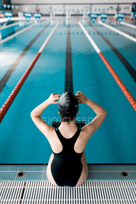Пловец сидит на краю бассейна и надевает очки для плавания — стоковое фото