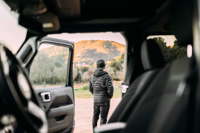Vista trasera a través del interior de un coche de un hombre contemplando el paisaje montañoso al amanecer - foto de stock
