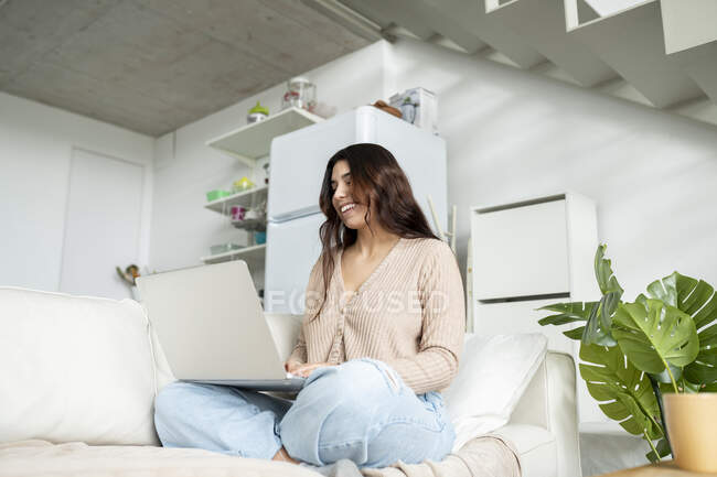 Знизу жінка переглядає Інтернет на портативному комп'ютері, відпочиваючи на дивані вдома — стокове фото