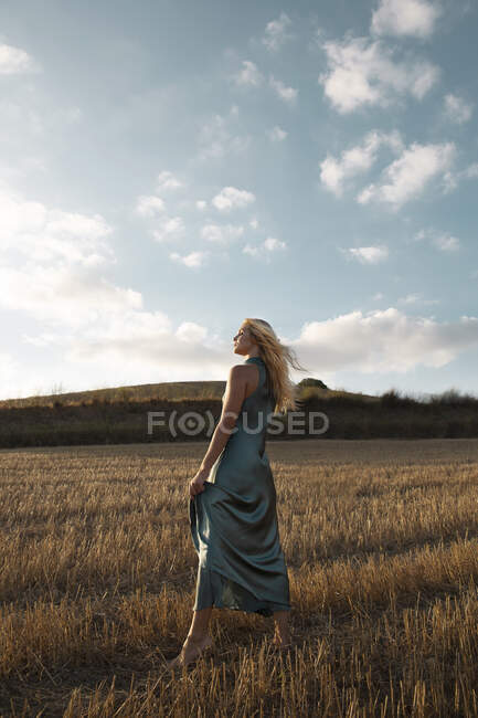 Mulher pacífica em vestido elegante em pé no campo seco na área rural e olhos fechados — Fotografia de Stock