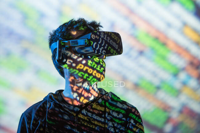 Unrecognizable bearded male in hoodie and modern headset exploring virtual reality in neon light — Stock Photo
