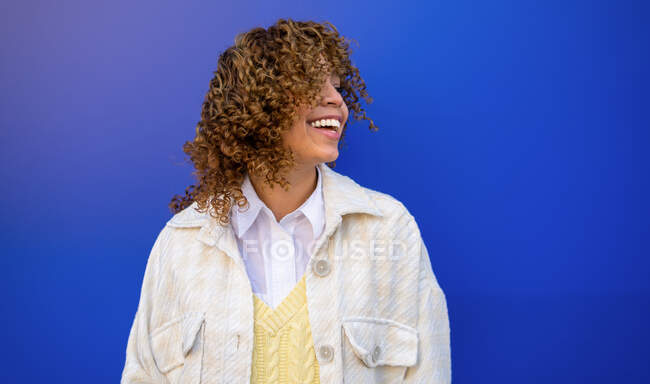 Mulher afro-americana encantada com penteado encaracolado voador em pé no fundo azul no estúdio — Fotografia de Stock