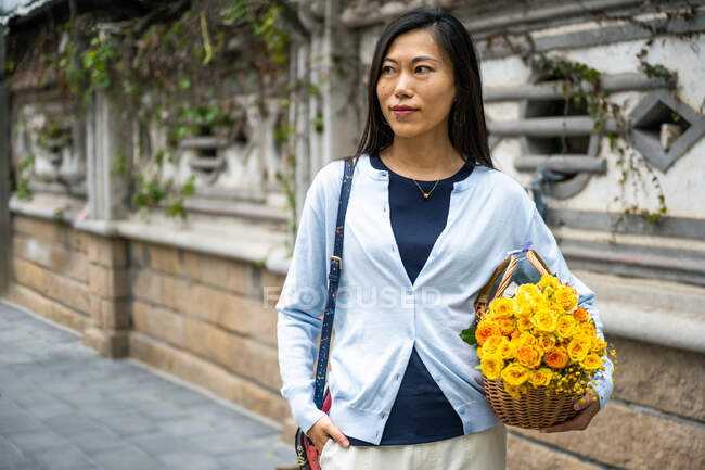 Hermosa chica asiática retrato mientras ella lleva una canasta de mimbre con flores amarillas. - foto de stock
