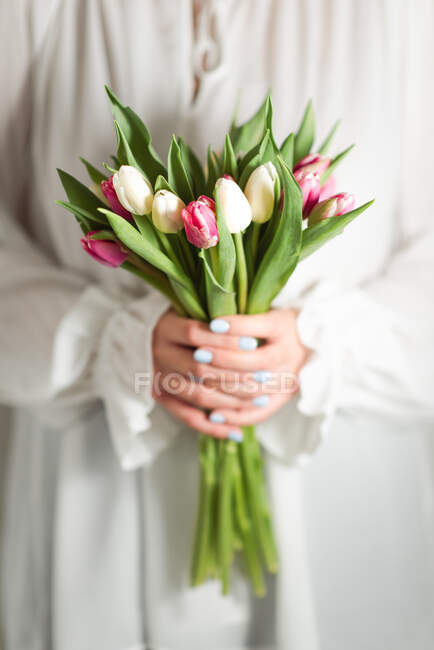 Crop unrecognizable female in romantic dress standing with bunch of tender colorful flowers — Stock Photo
